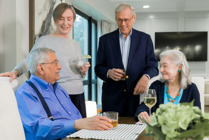 Four people gather around a table, enjoying drinks and conversation in a comfortable, modern dining room with a large window.