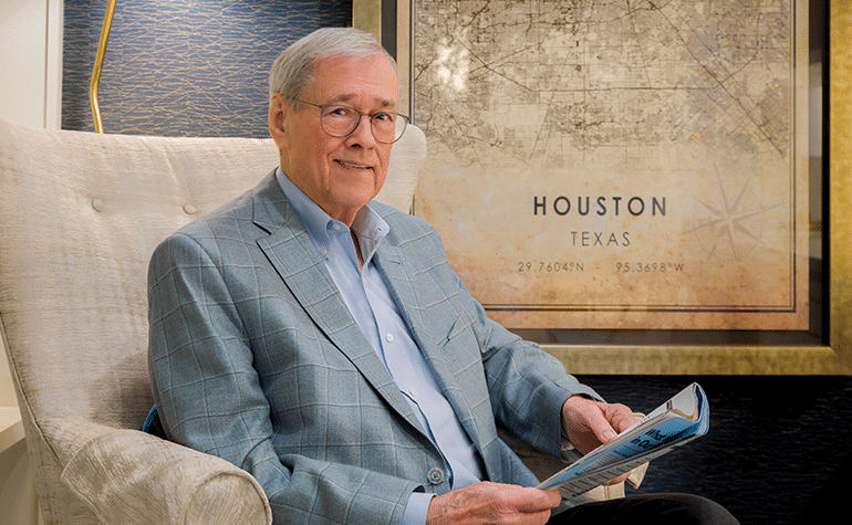 A person sits in a chair holding a magazine, with a decorative map of Houston, Texas, in the background.