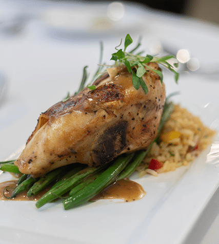 A perfectly roasted chicken breast on a bed of green beans, garnished with fresh herbs, served with rice and vegetables on a rectangular plate.