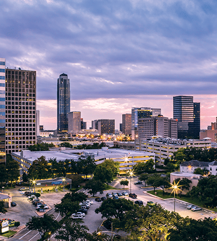 The image shows a skyline view of Houston, Texas at sunset, featuring tall buildings and busy streets illuminated by city lights.