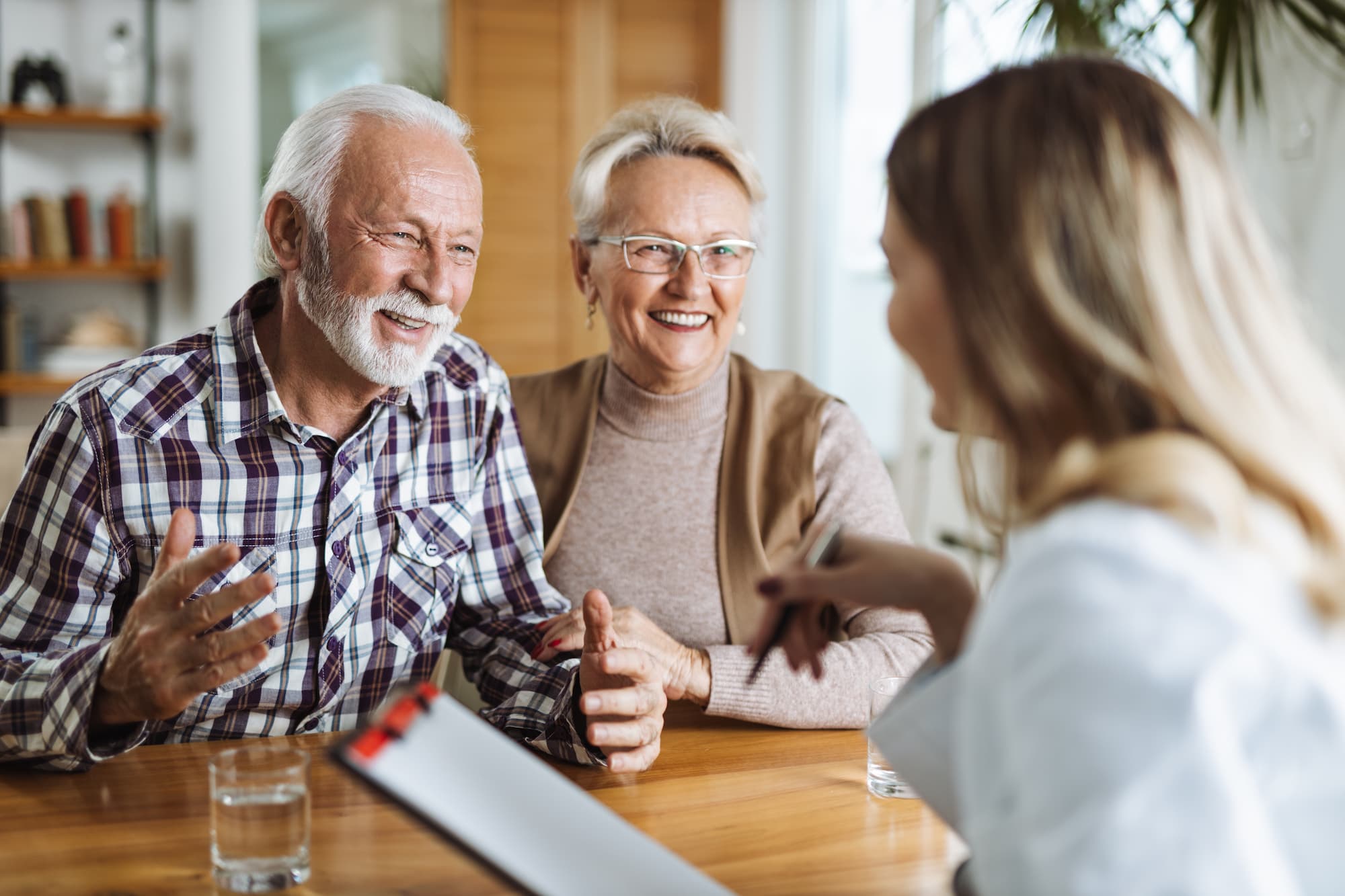 A senior couple of a man and woman smiling as they sit across the table from an adult woman with a checkboard as they discuss