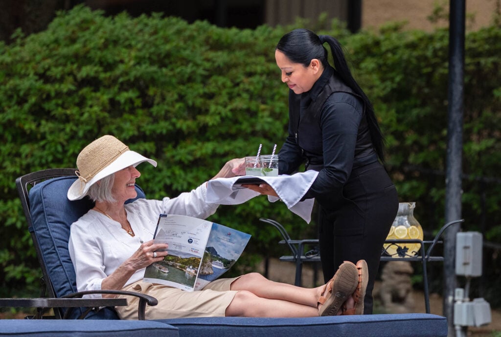 senior woman receives drink service by the poolside.