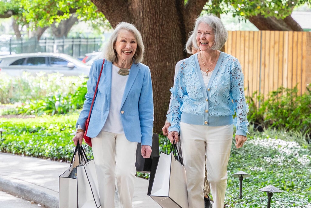 two senior women walking through the outdoor park near The Hallmark, dressed in their Sunday finest.